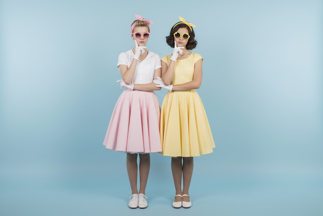 two teenage girls, vintage style 50's with pink and yellow sunglasses, arms looped together, each free arm is resting on the chin with their free arms slightly bent